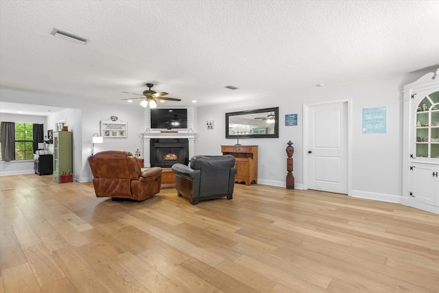200 Raintree Trl, Saint Augustine, FL 32086 - living room featuring light wood-type flooring, a textured ceiling, a ceiling fan, and a lit fireplace