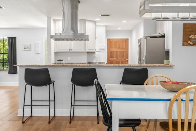 200 Raintree Trl, Saint Augustine, FL 32086 - kitchen with freestanding refrigerator, wall chimney range hood, white cabinetry, a kitchen breakfast bar, and recessed lighting