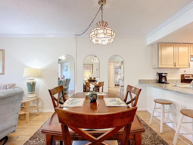 dining room with ornamental molding, a textured ceiling, sink, an inviting chandelier, and light hardwood / wood-style floors