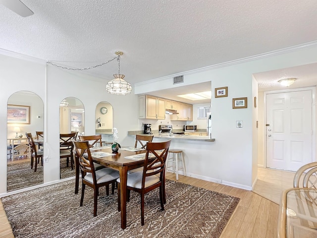 dining area featuring light wood-type flooring, a textured ceiling, and ornamental molding