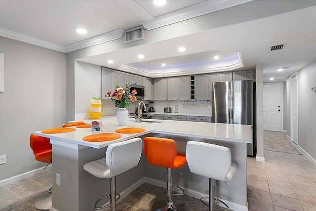 kitchen with sink, tasteful backsplash, appliances with stainless steel finishes, a kitchen breakfast bar, and kitchen peninsula