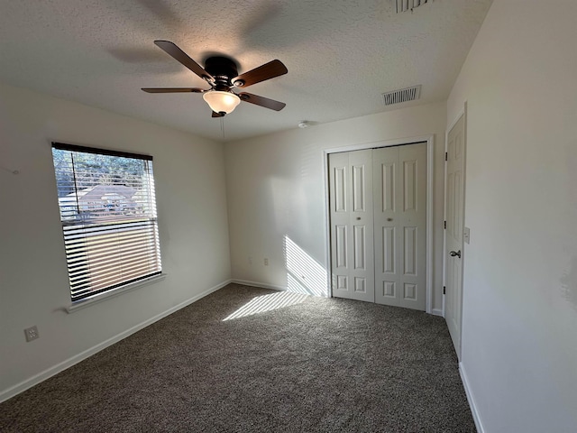 unfurnished bedroom featuring a textured ceiling, dark colored carpet, a closet, and ceiling fan