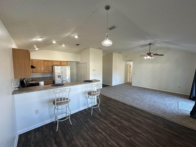 kitchen featuring vaulted ceiling, kitchen peninsula, white refrigerator with ice dispenser, a breakfast bar area, and a textured ceiling