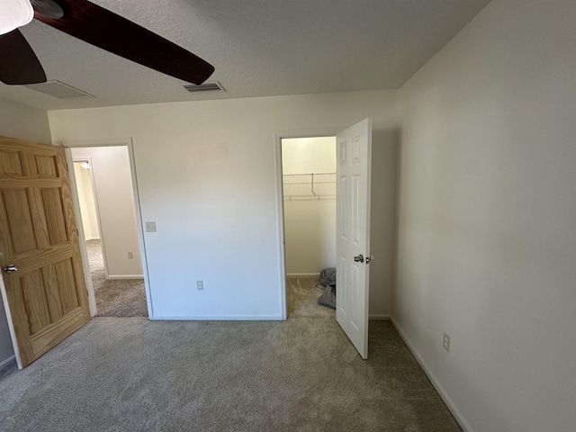 unfurnished bedroom with ceiling fan, a walk in closet, a closet, and carpet