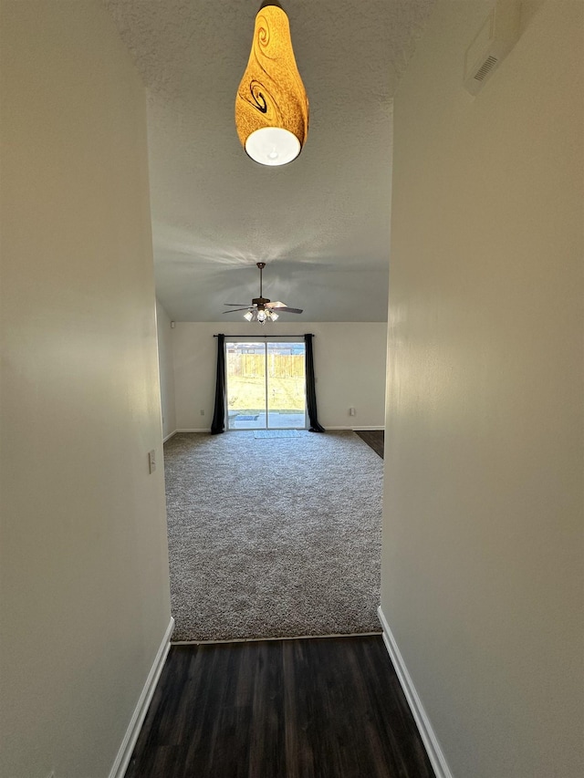 corridor with a textured ceiling and dark colored carpet