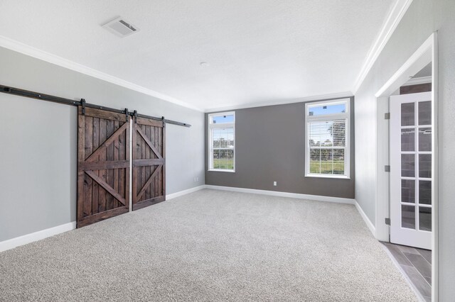 unfurnished room with light carpet, a textured ceiling, a barn door, and ornamental molding