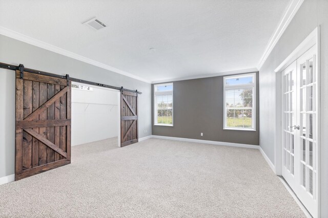 carpeted empty room with a barn door, ornamental molding, and french doors