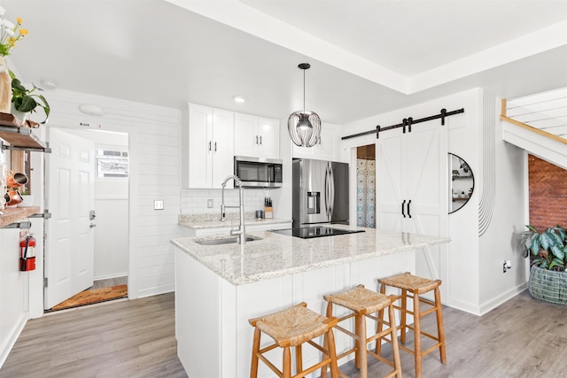 kitchen with appliances with stainless steel finishes, decorative light fixtures, sink, white cabinets, and a barn door