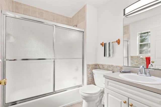 full bathroom featuring bath / shower combo with glass door, vanity, toilet, and tile walls