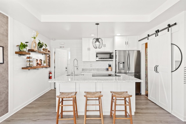 kitchen with sink, white cabinets, light stone counters, stainless steel appliances, and a barn door