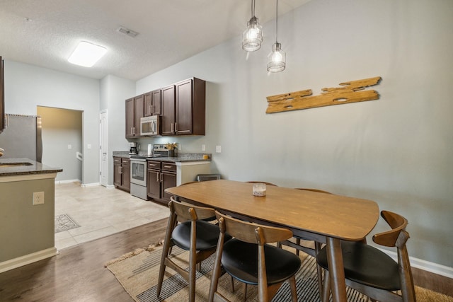 kitchen with pendant lighting, a textured ceiling, light hardwood / wood-style floors, dark brown cabinetry, and stainless steel appliances