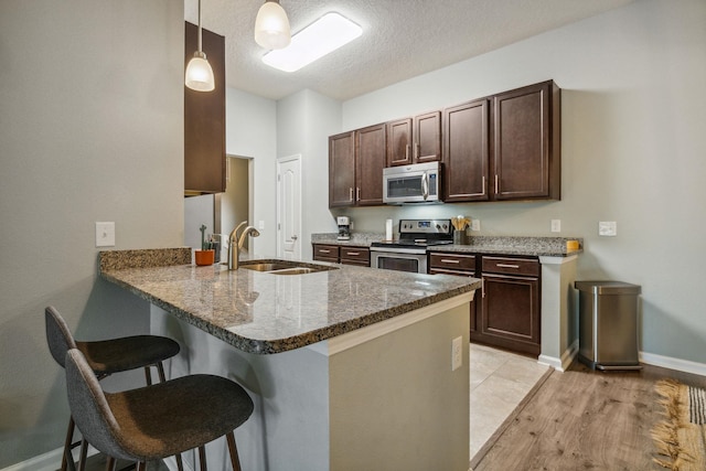 kitchen featuring a breakfast bar area, light wood-type flooring, decorative light fixtures, kitchen peninsula, and stainless steel appliances