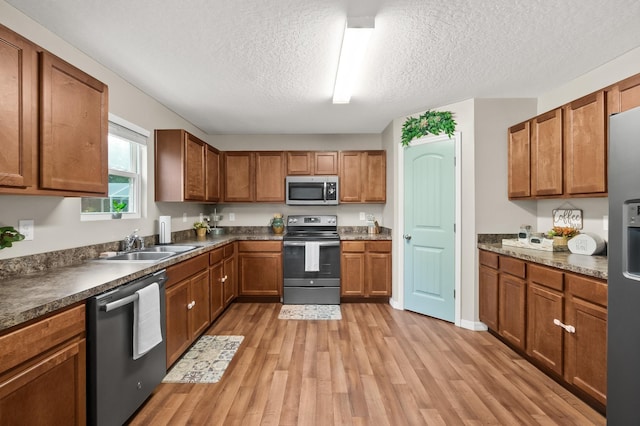 kitchen featuring appliances with stainless steel finishes, a textured ceiling, light hardwood / wood-style flooring, and sink