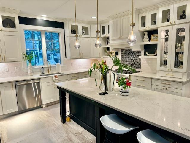 kitchen featuring glass insert cabinets, appliances with stainless steel finishes, hanging light fixtures, white cabinetry, and a sink