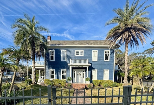 view of front of home featuring a balcony, a fenced front yard, a chimney, roof with shingles, and a gate