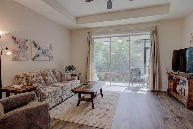 living room featuring hardwood / wood-style flooring, ceiling fan, and a raised ceiling