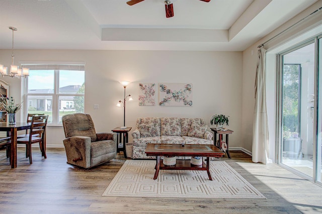 living room featuring ceiling fan with notable chandelier, hardwood / wood-style flooring, and a tray ceiling