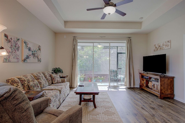 living room featuring a raised ceiling, ceiling fan, and wood-type flooring