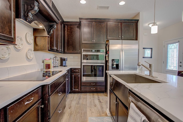 kitchen featuring light stone counters, dark brown cabinets, stainless steel appliances, light hardwood / wood-style flooring, and hanging light fixtures