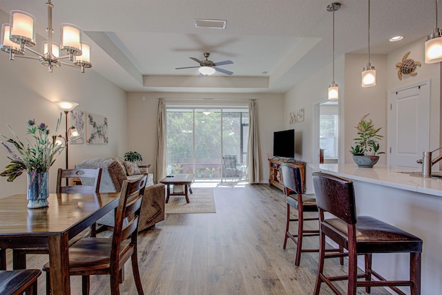 dining space featuring a raised ceiling, ceiling fan with notable chandelier, and hardwood / wood-style flooring