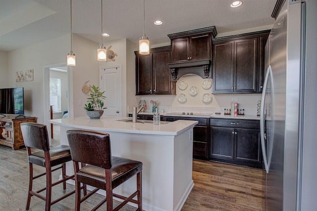 kitchen featuring decorative light fixtures, an island with sink, and stainless steel refrigerator