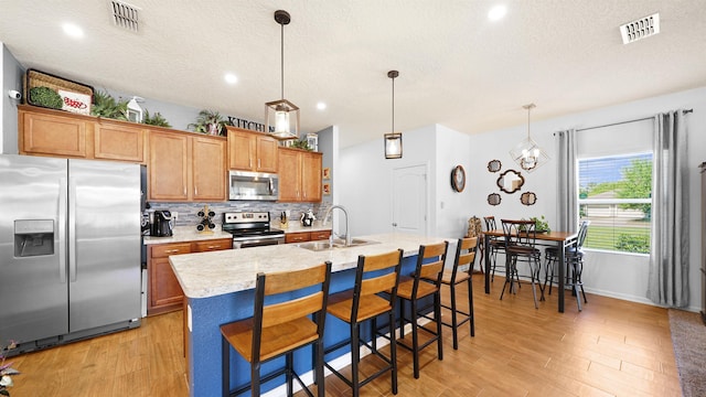 kitchen featuring pendant lighting, a kitchen bar, light wood-type flooring, and appliances with stainless steel finishes