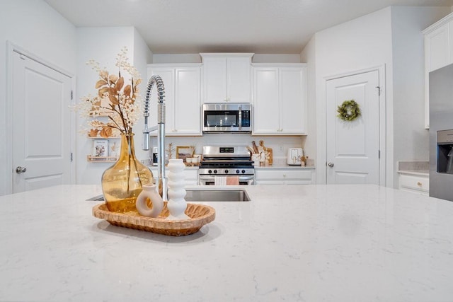 kitchen with light stone countertops, white cabinetry, and stainless steel appliances