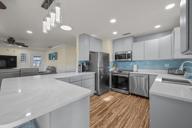 kitchen with stainless steel appliances, a peninsula, wood finished floors, a sink, and light countertops