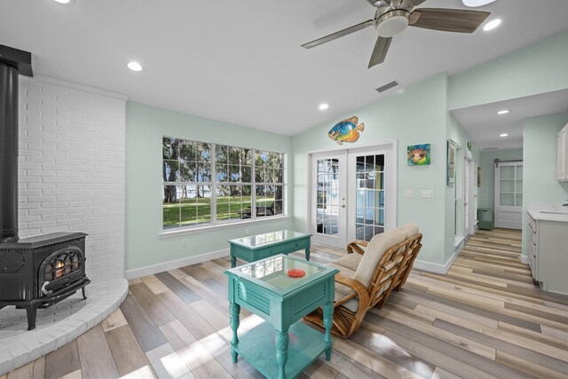 living room featuring lofted ceiling, a wood stove, french doors, ceiling fan, and light wood-type flooring