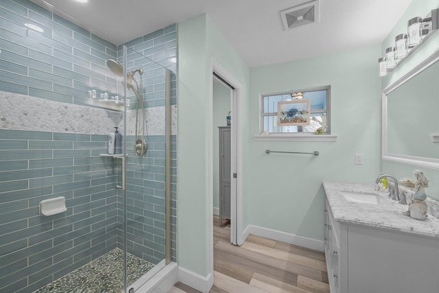 bathroom with a stall shower, baseboards, visible vents, wood finished floors, and vanity