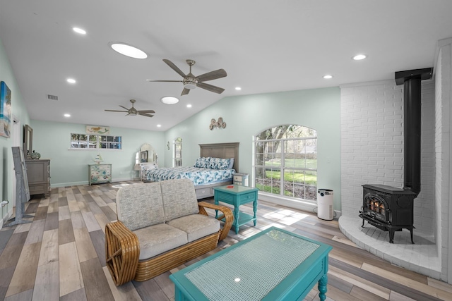 bedroom with visible vents, wood finished floors, a wood stove, vaulted ceiling, and recessed lighting