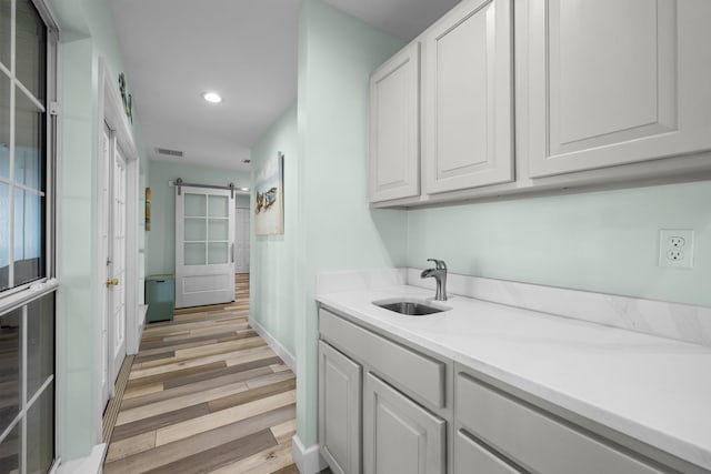 interior space with a barn door, white cabinetry, sink, and light hardwood / wood-style flooring