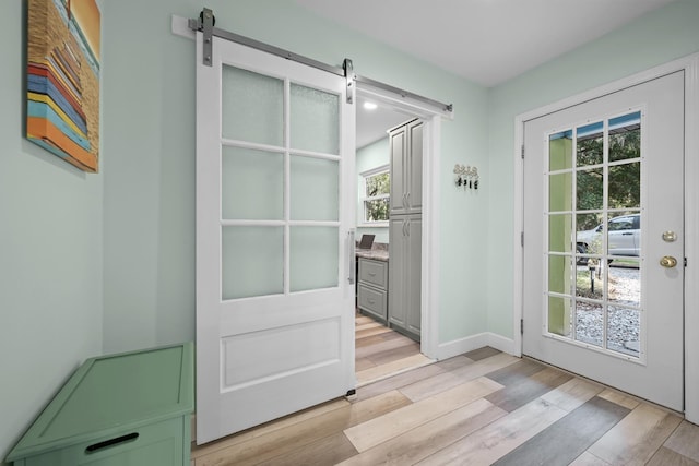 entryway with light wood-style floors, a barn door, and baseboards