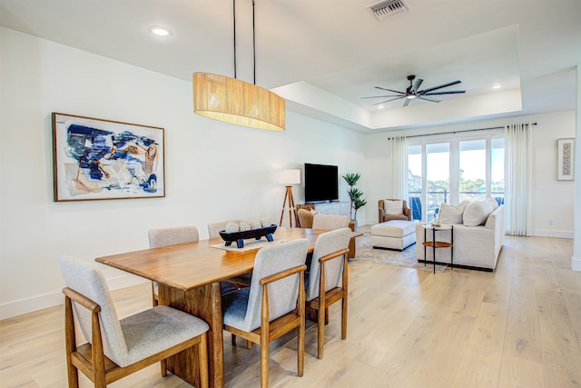 dining area featuring ceiling fan, light hardwood / wood-style floors, and a tray ceiling