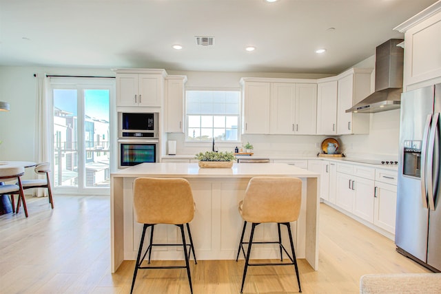 kitchen featuring appliances with stainless steel finishes, a center island, wall chimney range hood, and white cabinets