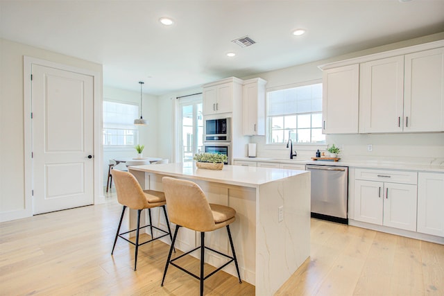 kitchen featuring a kitchen island, appliances with stainless steel finishes, pendant lighting, white cabinets, and light hardwood / wood-style floors