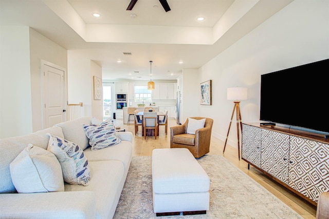 living room with light hardwood / wood-style flooring, a raised ceiling, and ceiling fan