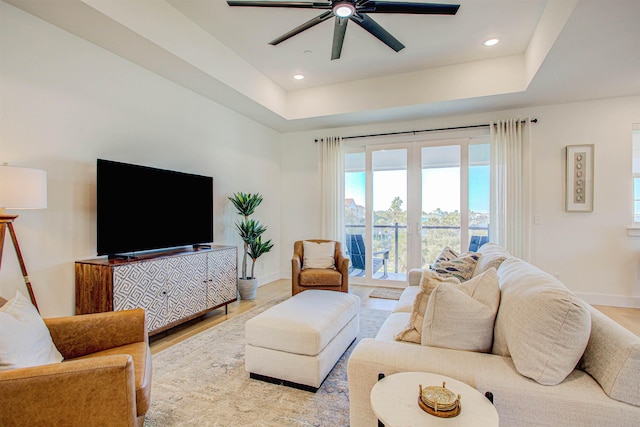 living room with ceiling fan, a tray ceiling, and light wood-type flooring