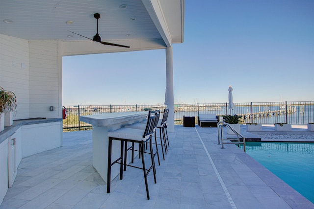 view of patio with a water view, ceiling fan, exterior bar, and a fenced in pool