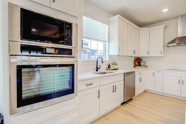 kitchen featuring sink, wall chimney range hood, black appliances, light hardwood / wood-style floors, and white cabinets