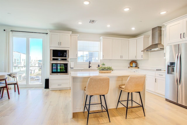 kitchen featuring white cabinets, a center island, stainless steel fridge with ice dispenser, light wood-type flooring, and wall chimney exhaust hood