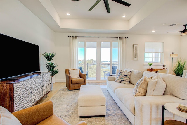 living room with light hardwood / wood-style floors, a raised ceiling, and ceiling fan