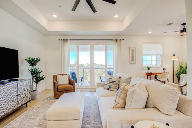 living room with a raised ceiling, light wood-type flooring, and ceiling fan