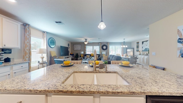 kitchen featuring ceiling fan with notable chandelier, light stone counters, white cabinetry, and hanging light fixtures