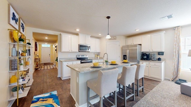 kitchen with light stone countertops, stainless steel appliances, pendant lighting, a center island with sink, and white cabinets