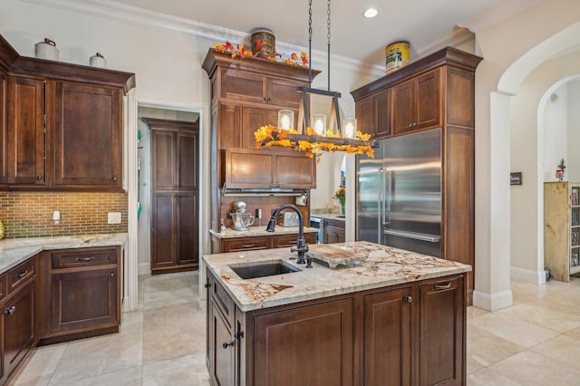 kitchen featuring a center island with sink, built in refrigerator, ornamental molding, and sink