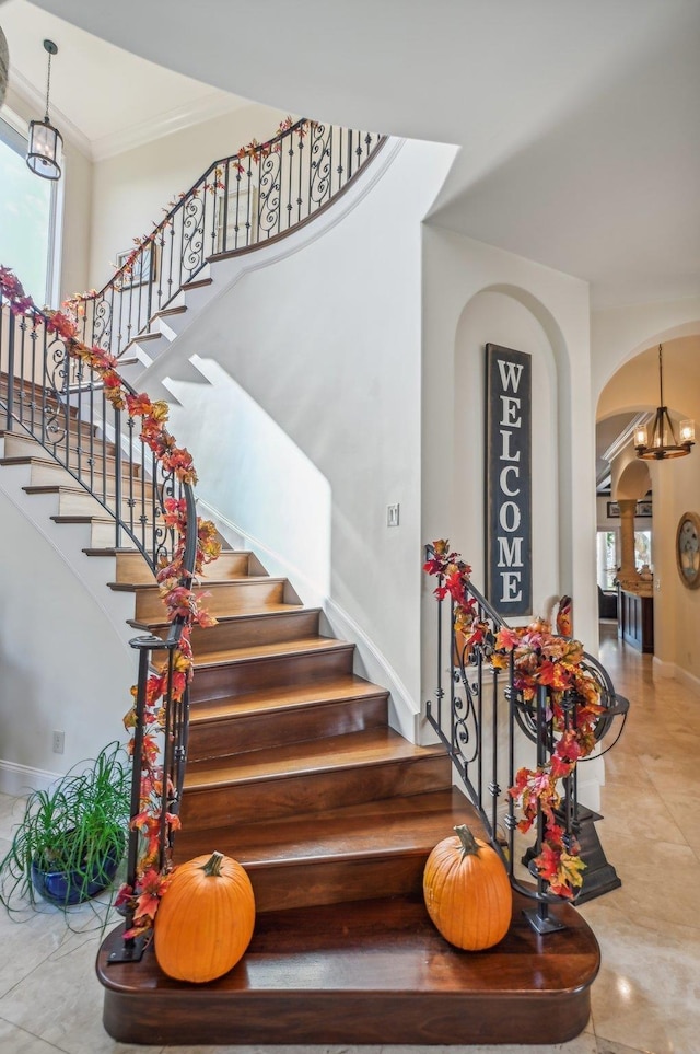 staircase with crown molding, a wealth of natural light, and a notable chandelier