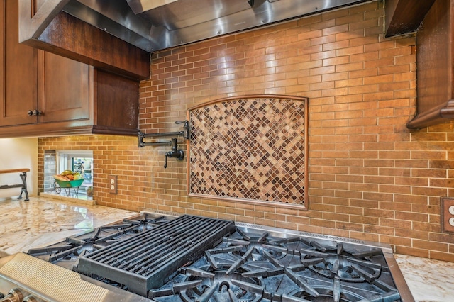 kitchen featuring light stone counters, black gas stovetop, and brick wall