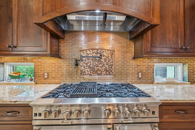 kitchen featuring decorative backsplash, a healthy amount of sunlight, light stone countertops, and stainless steel range