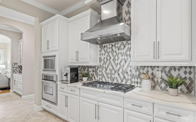 kitchen with wall chimney exhaust hood, decorative backsplash, light tile patterned floors, white cabinetry, and stainless steel appliances